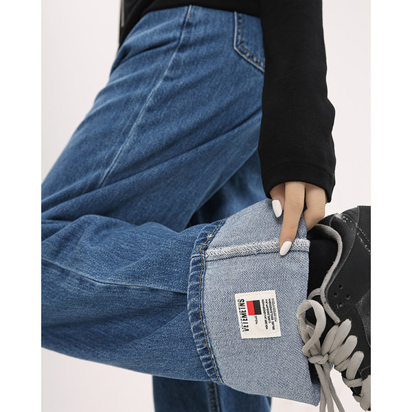 Sirge kõrge vöökohaga naiste teksapükste mudel, mille ühel säärel on embleem