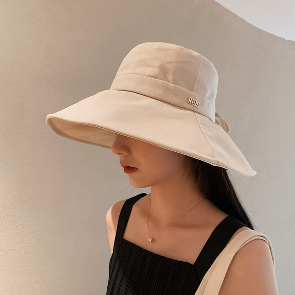 Naiste tekstiilist müts laia ääre ja metallist pealdisega